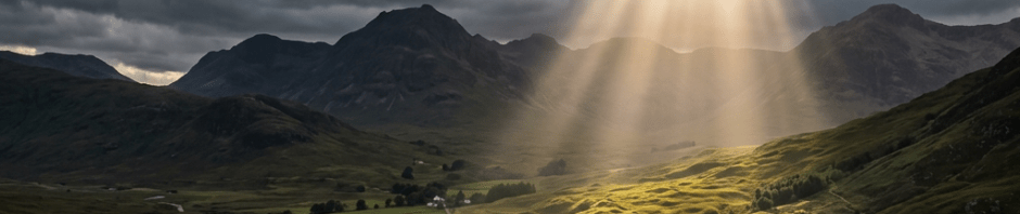 Sunlight shines through dark clouds onto a lush valley with winding river and distant mountains